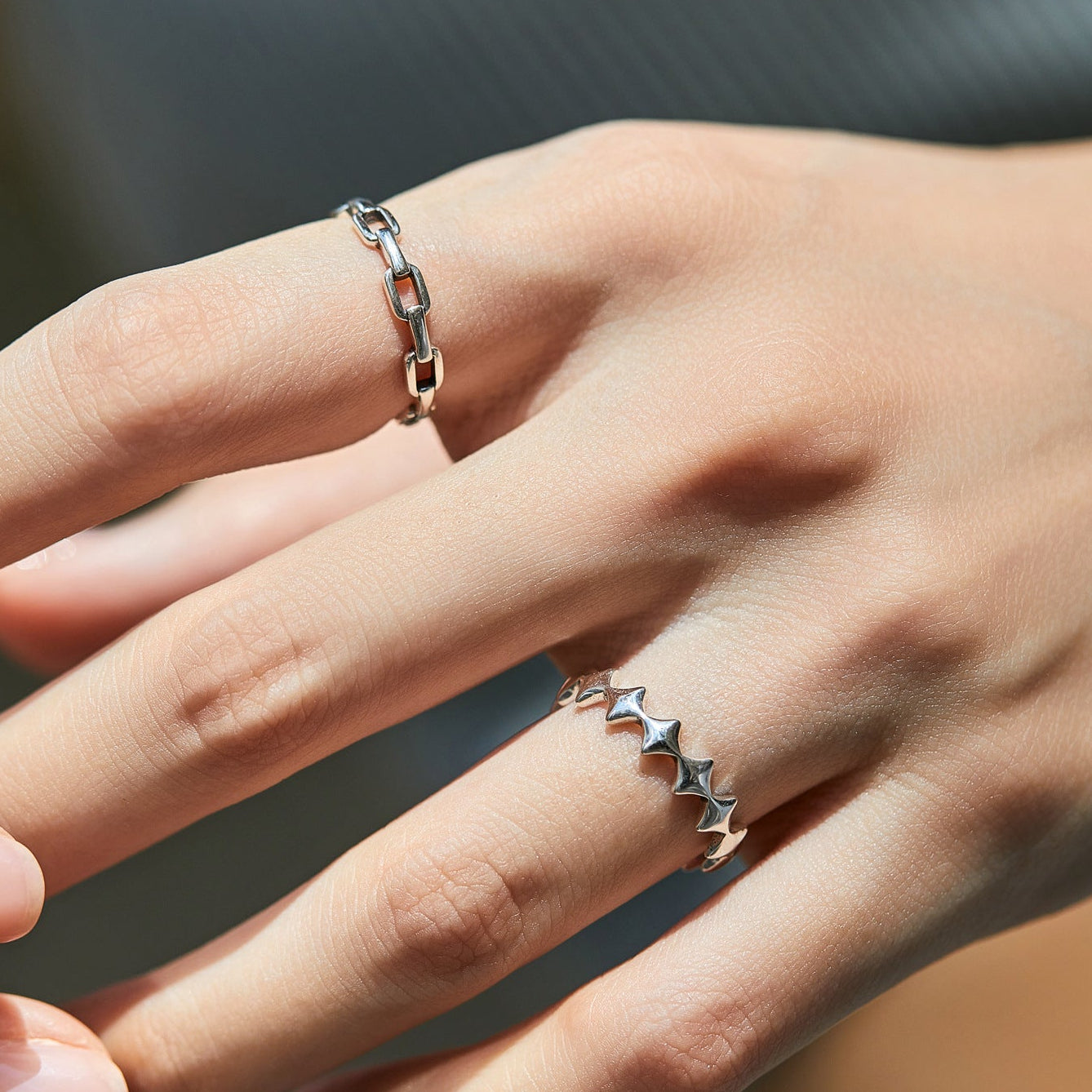 Close-up of a hand wearing two silver rings with star designs on a dark background.